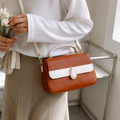 Person holding a brown handbag with a white stripe, wearing a white sweater and beige pants.